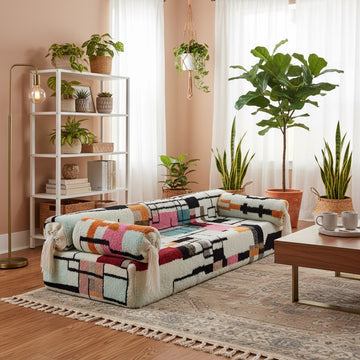 Living room with a colorful boho sofa  patterned sofa, plants, and a coffee table.